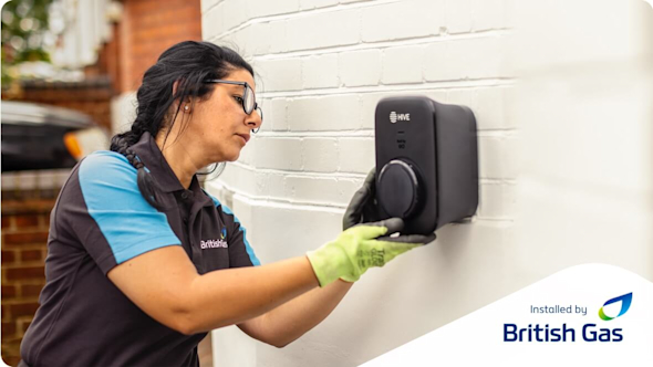 British Gas engineer installing a EO Mini Pro 3 charger on the wall of a white brick house with an Installed by British Gas logo in the bottom right corner