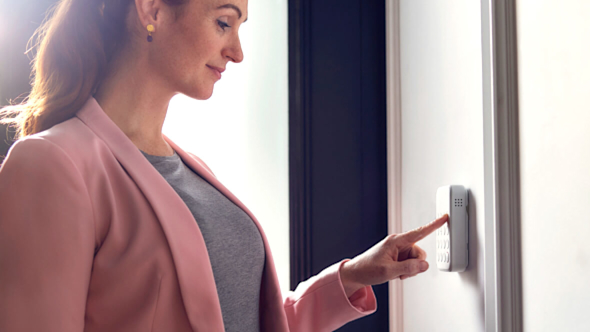 Woman in a pink blazer pressing a button on the Hive Keypad that's attached to a wall in a hallway