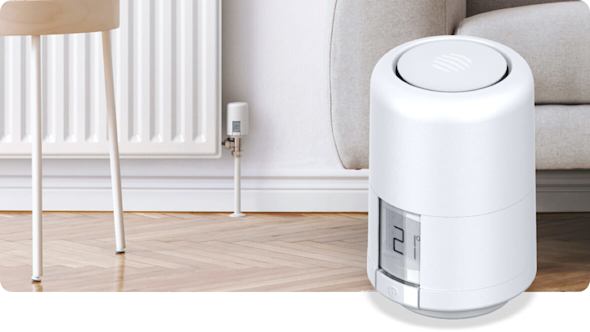 Modern living room showing a close-up of a white radiator with a Hive Radiator Valve attached to the side, with a wooden table in front and a grey sofa to the side, and a Hive Radiator Valve superimposed in the bottom right corner