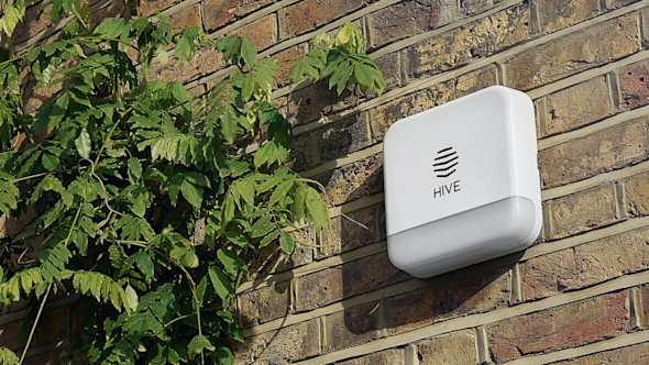 Hive Siren attached to a brown brick wall of a house with a green plant next to it on the left