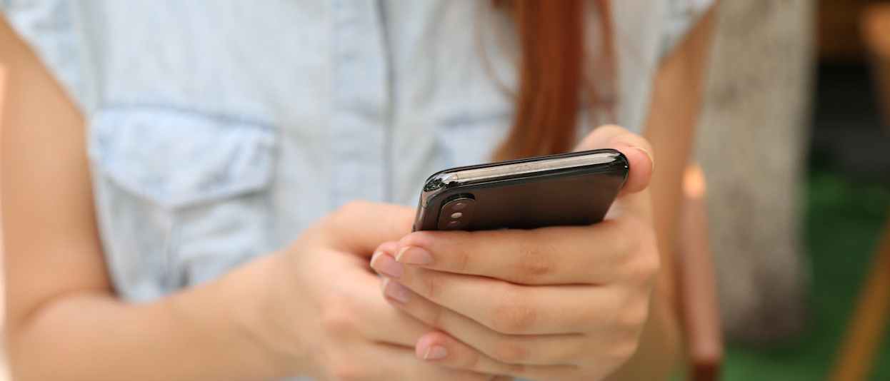 Close-up of a woman wearing a light blue shirt holding a smartphone with two hands