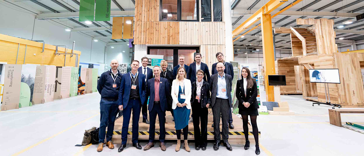 A group of well-dressed people standing in front of a wooden house in a warehouse