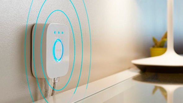Philips Hue Bridge hub, attached to a white painted wall, above a white and glass unit with blue circular lines superimposed over the top
