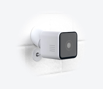 Side angle view of Hive View Outdoor Camera, attached to a white brick wall, on a white background