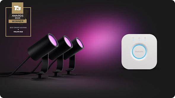 Composite image of Philips Hue Lily Outdoor Lights, showing a purple light, with a Philips Hue Bridge to the right of the image and a awards logo in the top left corner, all on a dark background