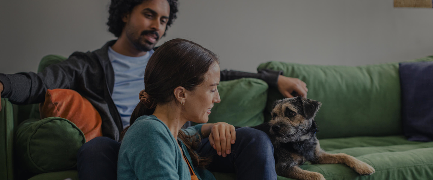Young dad looking at his smartphone while holding a small baby in his arms with a bright ceiling light and stripy wallpaper in the background