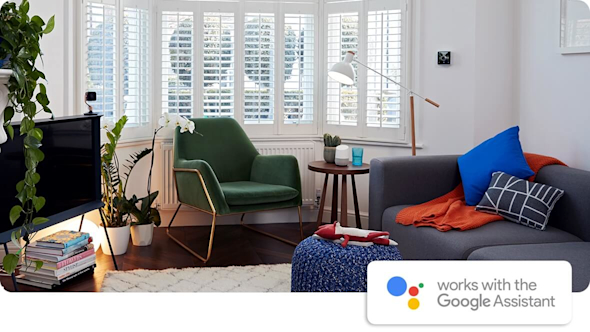 Modern living room with bay window, grey sofa, TV, fireplace, green armchair and Hive smart devices around the room