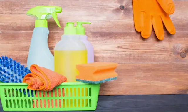 Cleaning supplies, including spray bottles, sponges, and gloves, neatly arranged on a wooden surface.