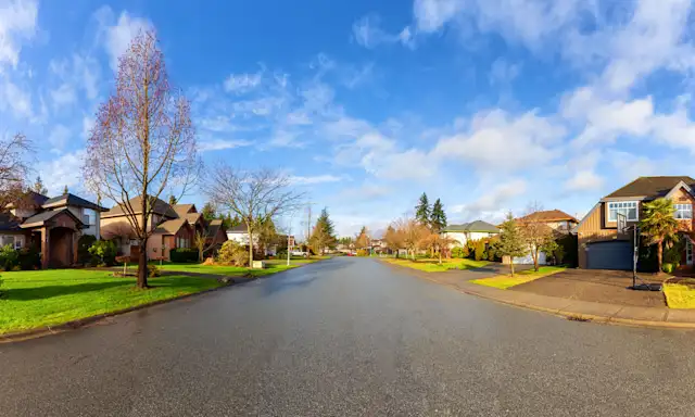 Quiet residential street in a suburban neighborhood in Surrey, British Columbia, with houses and trees under a blue sky.