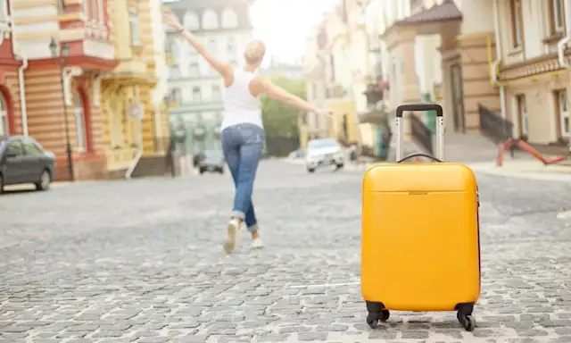 Yellow suitcase on cobblestone street with woman walking away joyfully