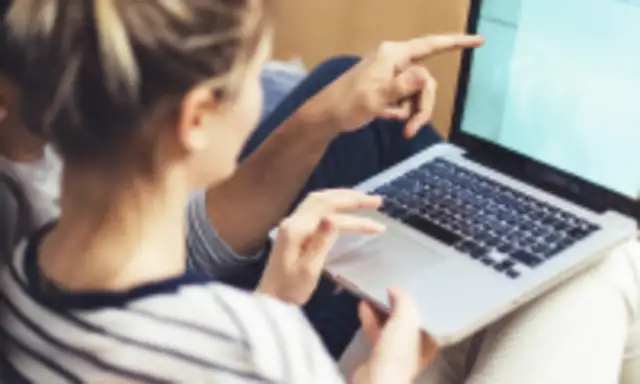 Couple sitting together and looking at a laptop screen with moving boxes in the background.