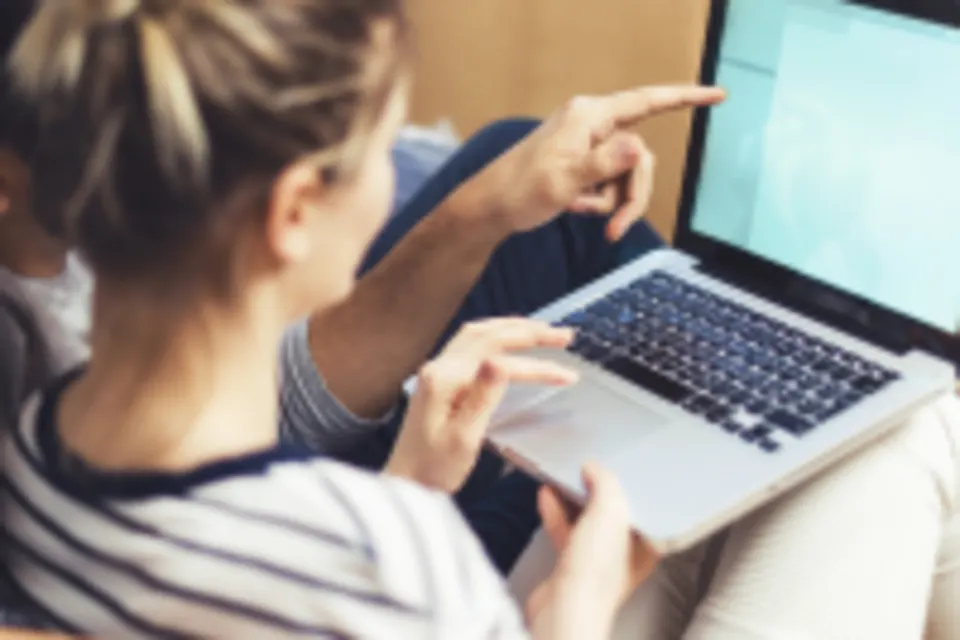 Couple sitting together and looking at a laptop screen with moving boxes in the background.