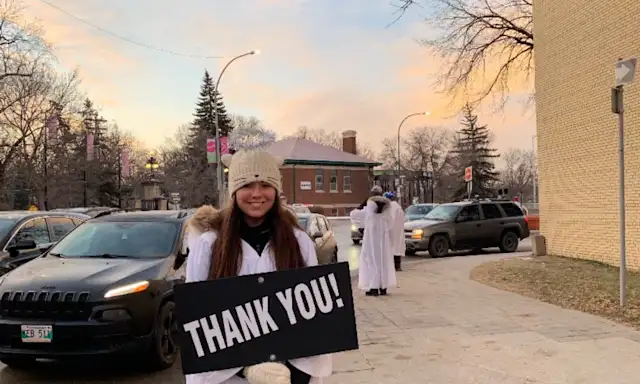 Person holding a 'Thank You!' sign on a sidewalk.