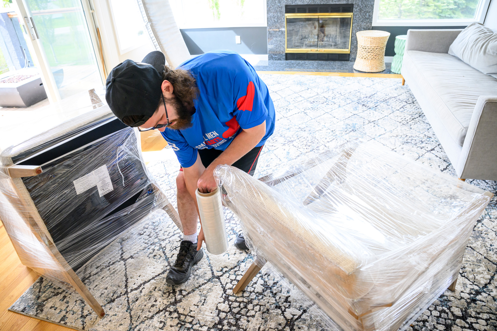 Man in a Two Small Men with Big Hearts Moving shirt wrapping furniture with protective plastic in a living room