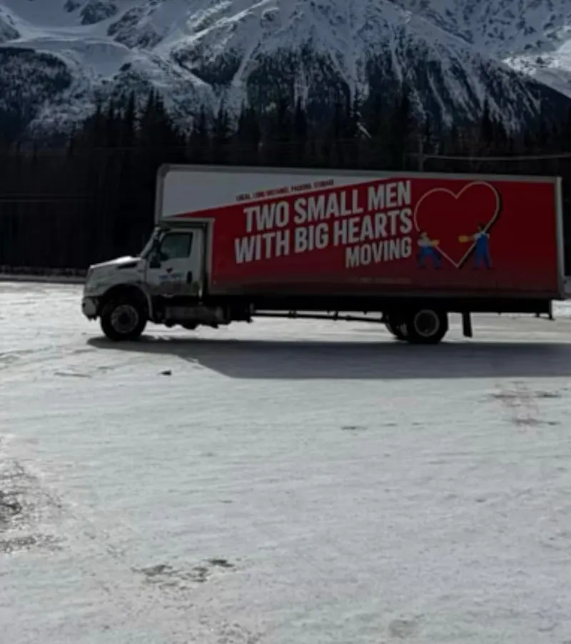 Two Small Men moving truck below snowy mountains