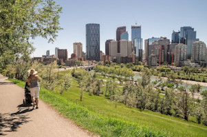 Person pushing a stroller along a path with the Calgary skyline in the background