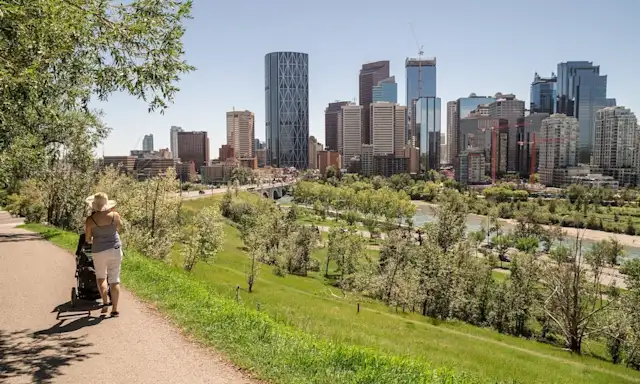 Person pushing a stroller along a path with the Calgary skyline in the background