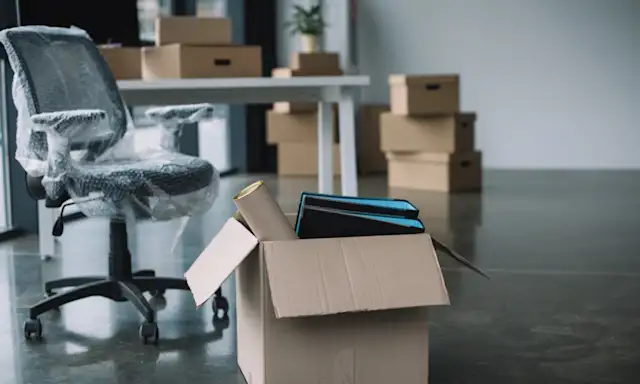 Office chair wrapped in plastic next to a packed box, with more boxes stacked in the background.