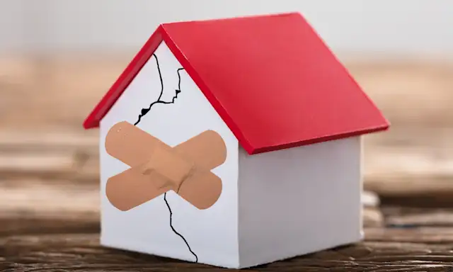 Model of a house with a crack on the wall, covered by two band-aids.