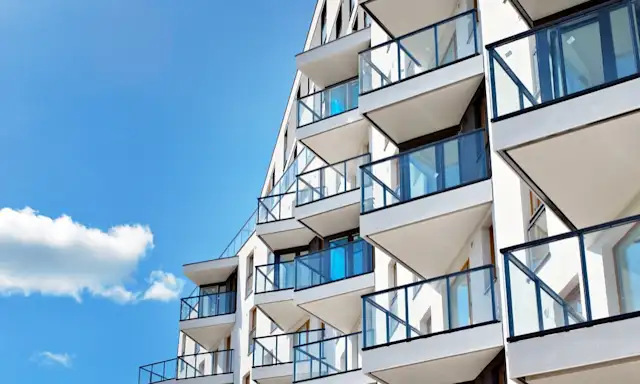 Modern apartment building with glass balconies under a blue sky.