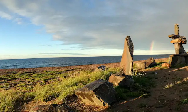 View of Hudson Bay from Churchill, Manitoba, with Inukshuk sculptures and a rainbow in the distance.