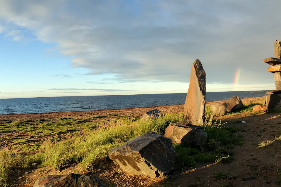 View of Hudson Bay from Churchill, Manitoba, with Inukshuk sculptures and a rainbow in the distance.