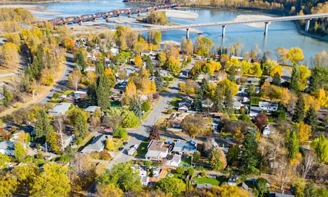 Aerial view of a neighbourhood in Prince George, with a river and a bridge in the background surrounded by autumn foliage.