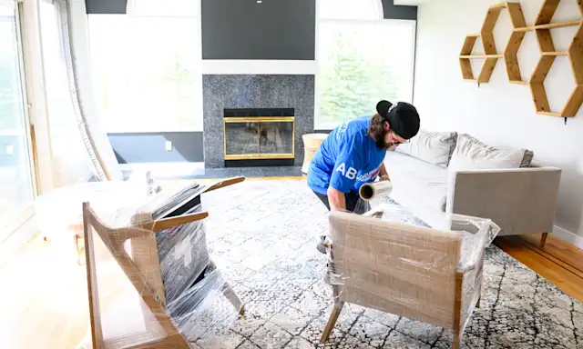 Mover from Two Small Men with Big Hearts Moving wrapping furniture with protective plastic in a living room.
