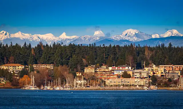 Scenic view of Comox, a coastal town with boats, surrounded by trees, with snow-capped mountains in the background.