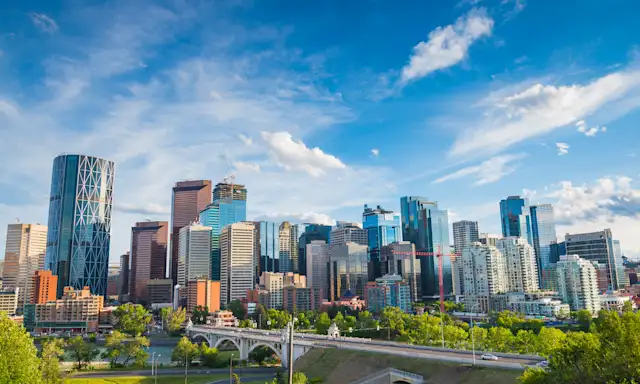 Cityscape of Calgary with modern skyscrapers and a bridge in the foreground on a clear day.