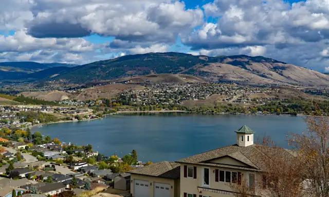 Aerial view of Vernon, British Columbia, with houses overlooking a lake and mountains in the background.
