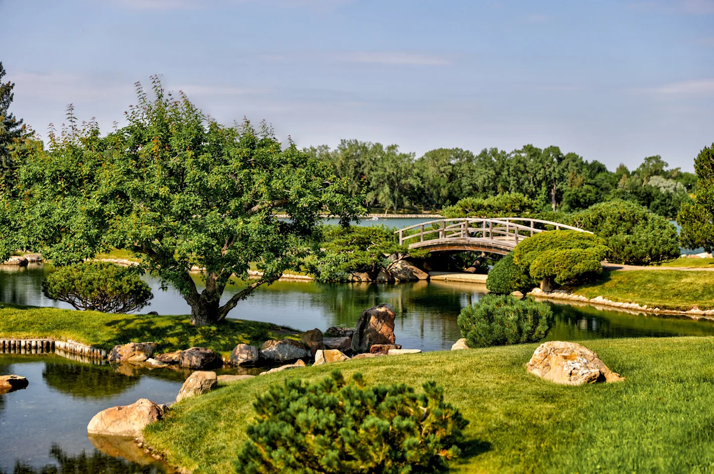 Scenic garden in Lethbridge featuring a wooden bridge over a pond surrounded by lush greenery.