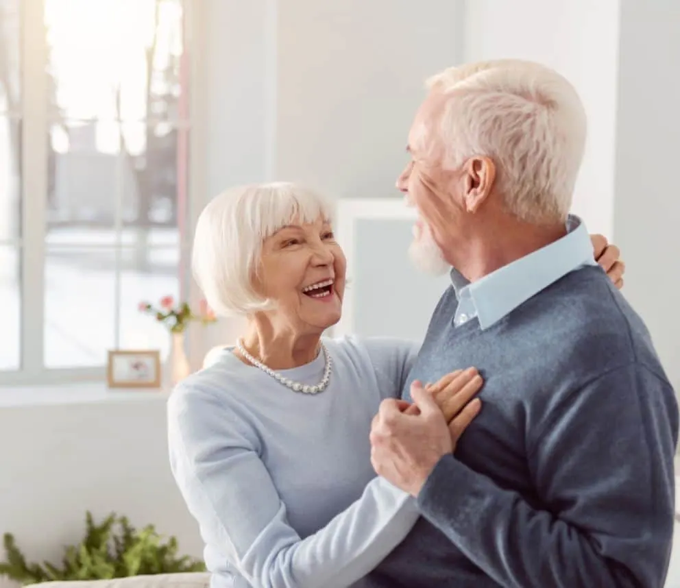 Happy elderly couple dancing together in a bright room.