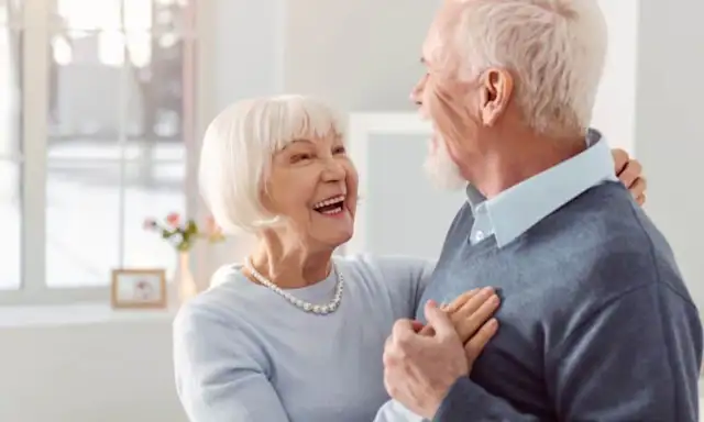 Happy elderly couple dancing together in a bright room.