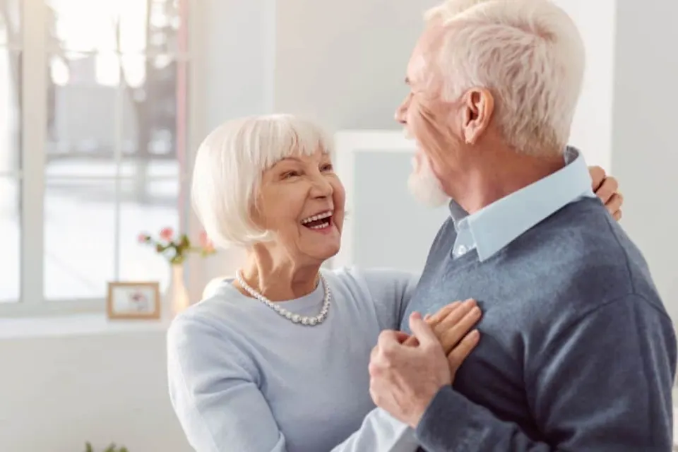 Happy elderly couple dancing together in a bright room.