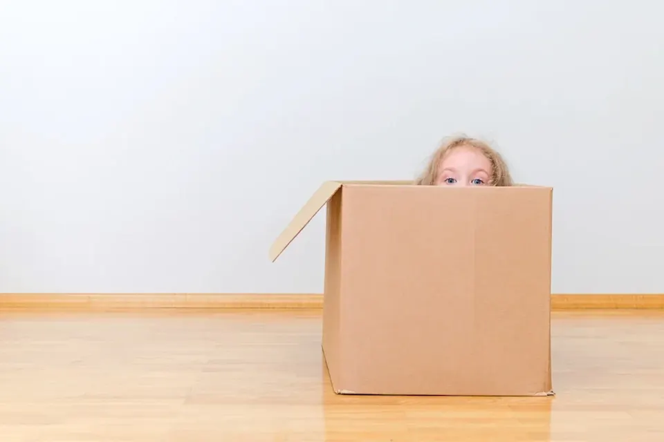 A playful moment during a move, with a child peeking out from inside a large cardboard box. The image captures the joy and lightheartedness of moving day.