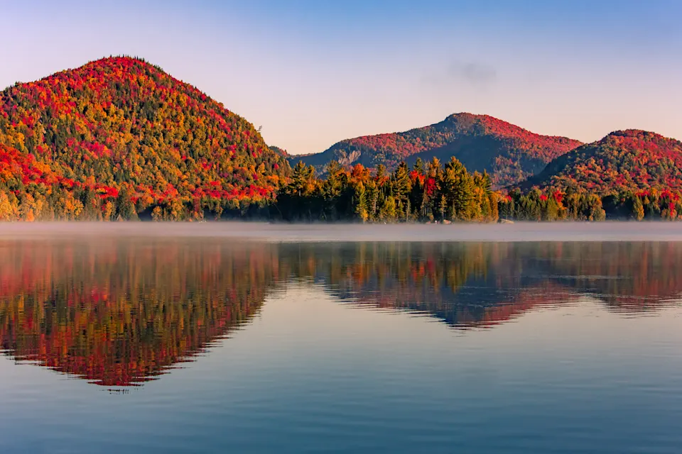 Autumn foliage reflecting on the calm waters of a lake in the Laurentian Mountains, Quebec, at sunrise.