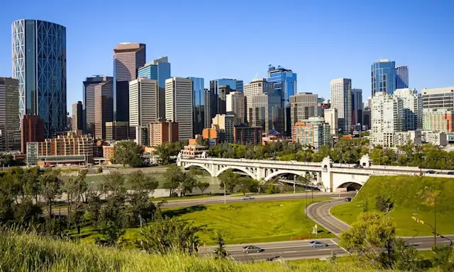 View of Calgary skyline with a bridge and green park in the foreground