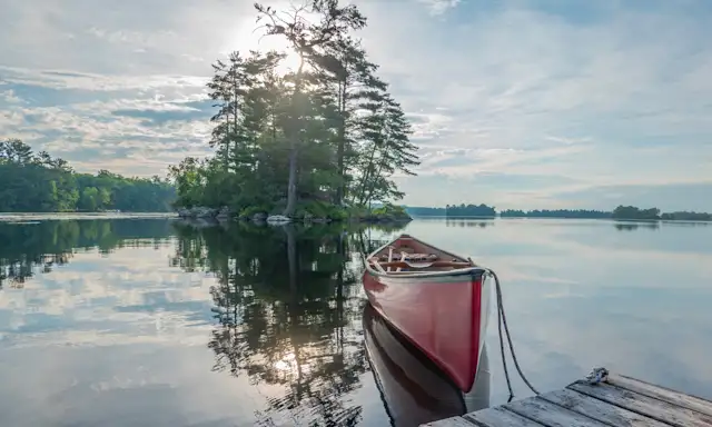 Red canoe tied to a dock on a calm lake with a small tree-covered island in Ontario.