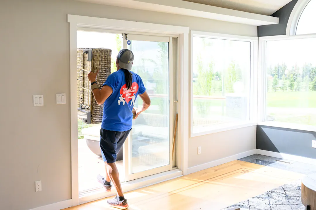 Mover from Two Small Men with Big Hearts Moving carrying furniture out of a house through a sliding door.