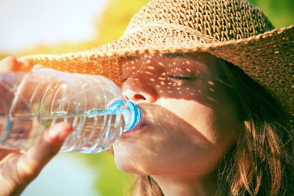 Person wearing a sun hat drinking water from a plastic bottle on a sunny day
