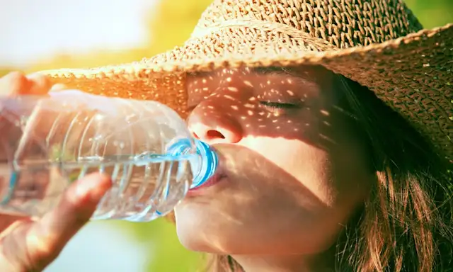 Person wearing a sun hat drinking water from a plastic bottle on a sunny day
