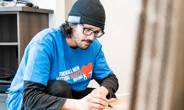 Man in a Two Small Men with Big Hearts Moving shirt labeling a moving box.