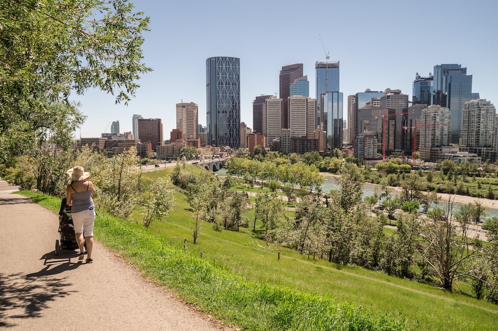 Person pushing a stroller along a path with the Calgary skyline in the background