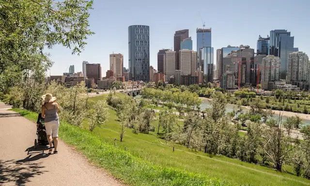 Person pushing a stroller along a path with the Calgary skyline in the background