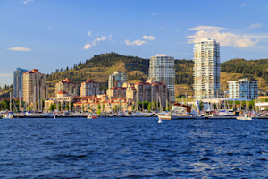 Waterfront view of Kelowna with high-rise buildings, marina, and hills in the background on a sunny day.