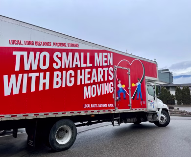 Two Small Men with Big Hearts Moving truck with branded signage and illustrations, parked on a street.
