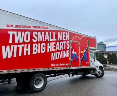 Two Small Men with Big Hearts Moving truck with branded signage and illustrations, parked on a street.