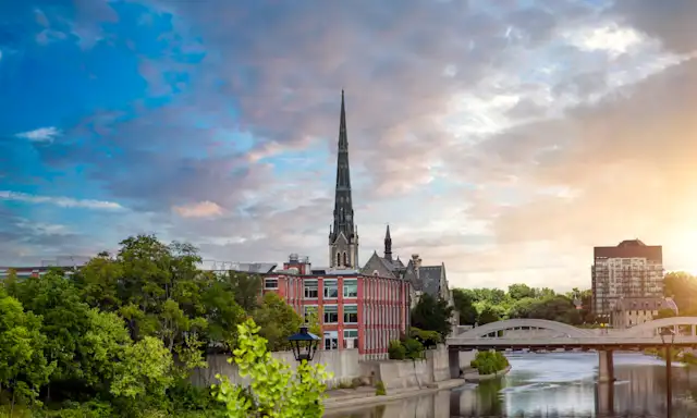 Scenic view of downtown Cambridge, Ontario, featuring a historic church and the Grand River at sunset.