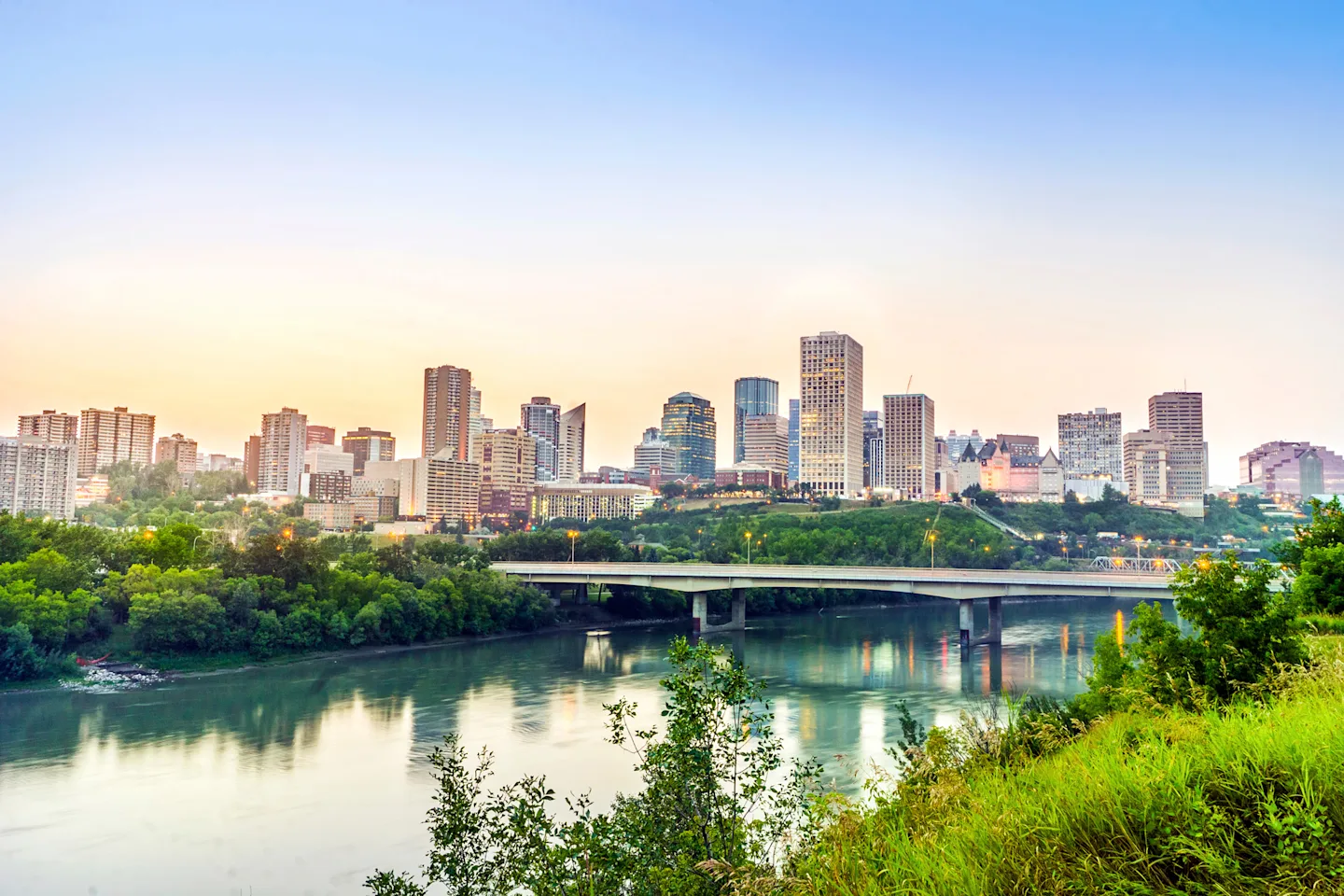 Edmonton city skyline at sunrise with the river and bridge in the foreground.